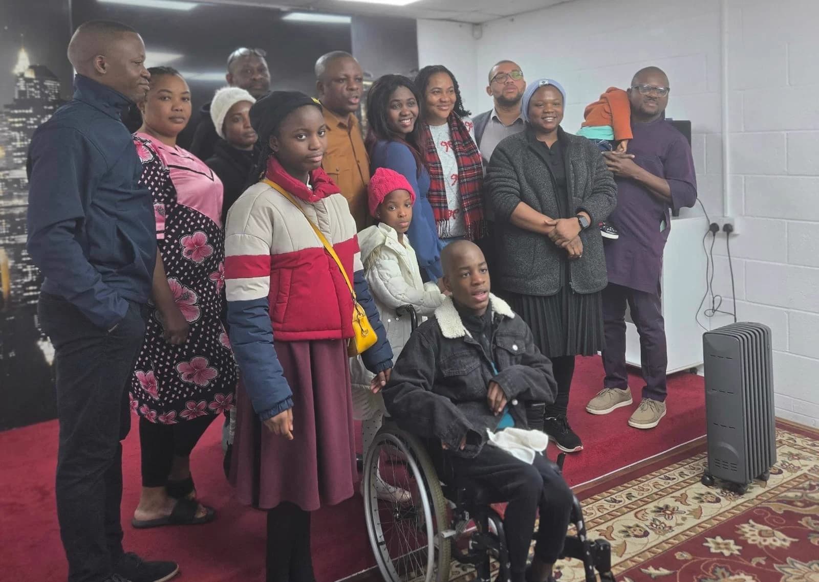Members of the congregation, adults and children, gathered together in the worship hall, a boy in a wheelchair at the front.