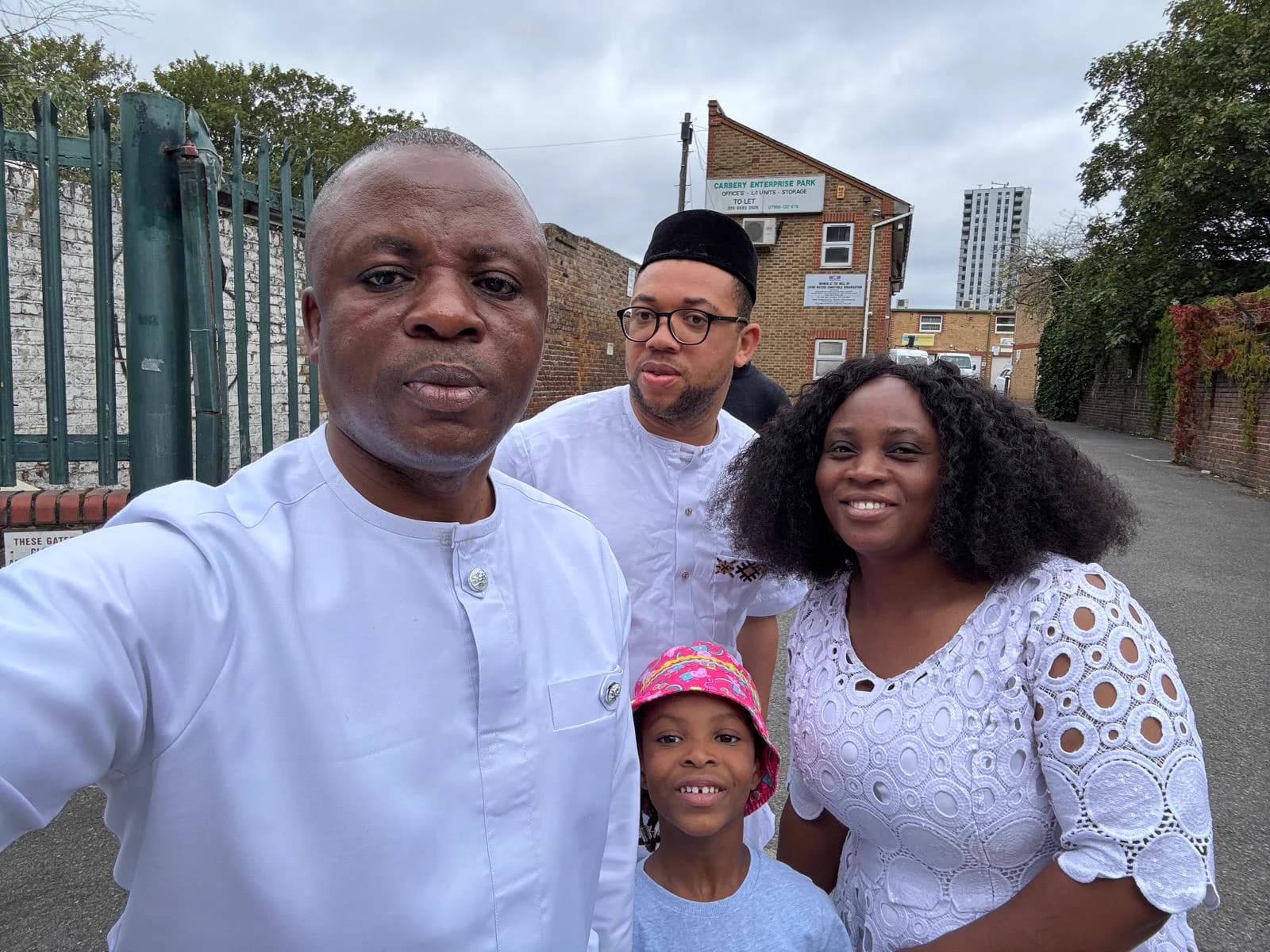 Kufre Okon, in white, taking a photograph with three others outside the gate on White Hart Lane, the Carbery Enterprise Park sign behind them.