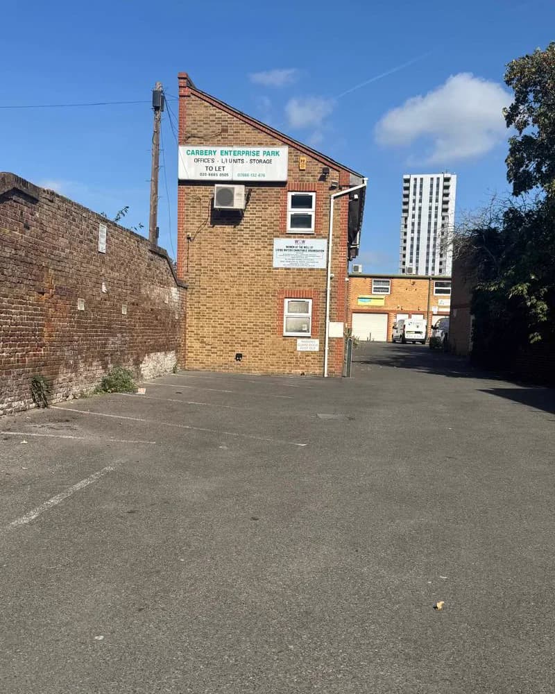 The compound at 36 White Hart Lane — the car park and the brick building that holds the worship hall, under a clear sky.