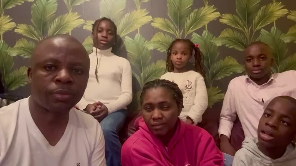 Kufre Okon and his family seated together on a sofa in front of palm-leaf wallpaper, looking to camera.