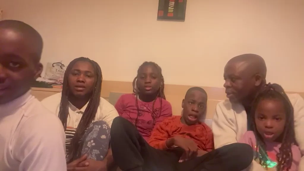 The minister's family gathered on a bed at home, children in the middle, all looking to camera.