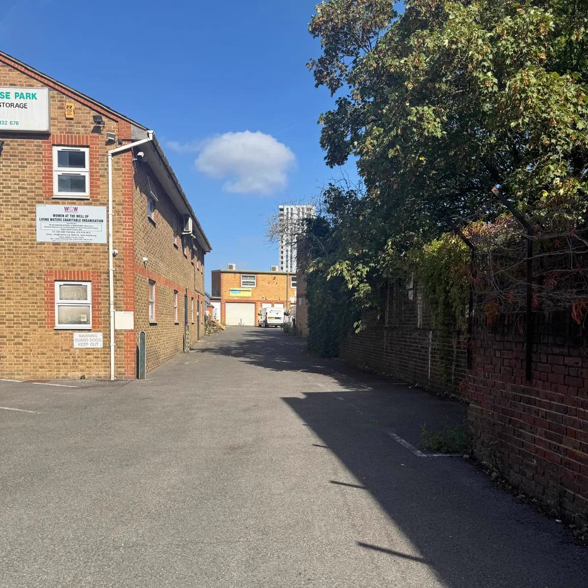 The approach outside the compound at 36 White Hart Lane — a tarmac lane running alongside the brick building, trees and a brick wall on the other side.