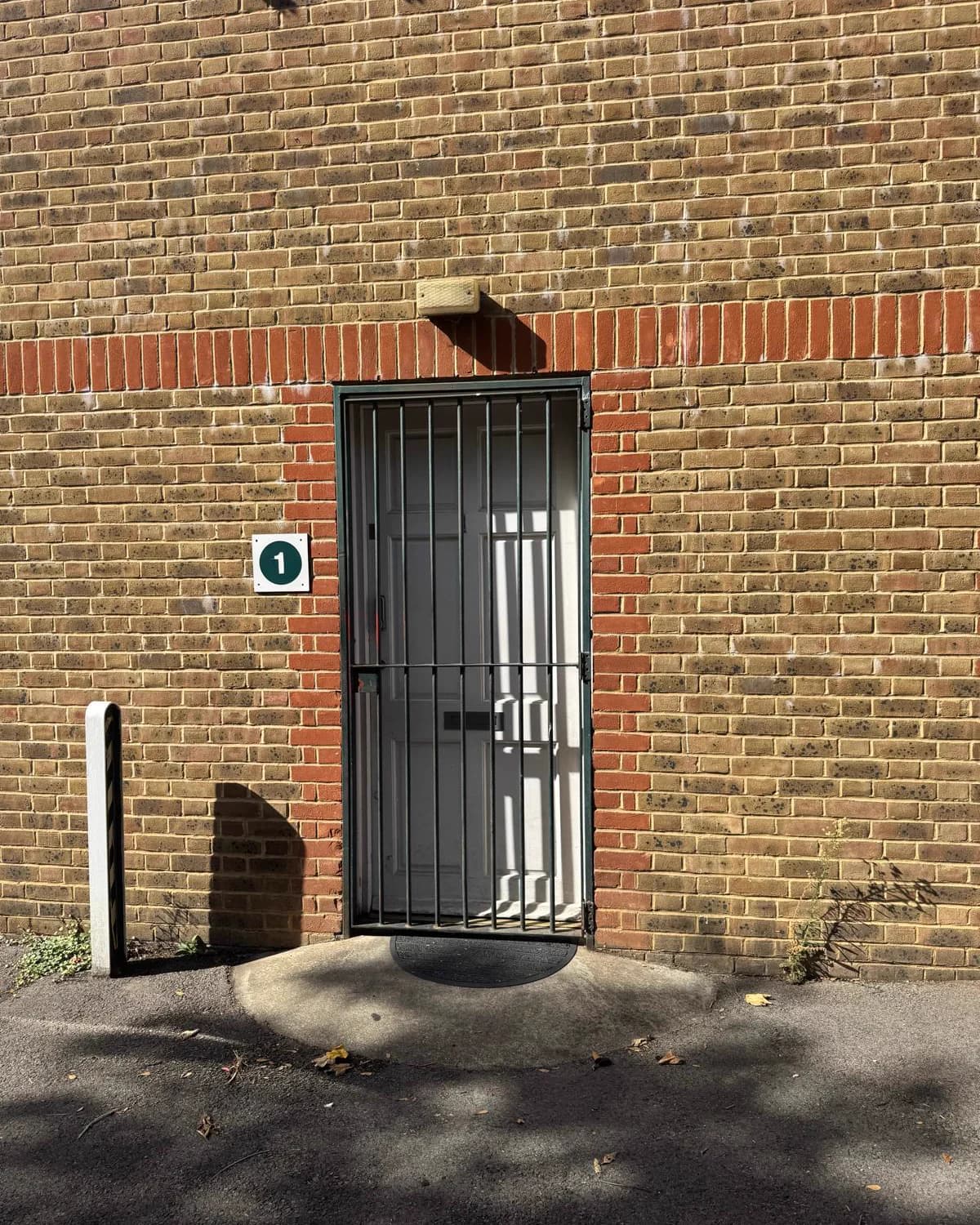 The door into the worship hall: a white door behind a green security gate, marked 1, with a step-free concrete ramp up to it.